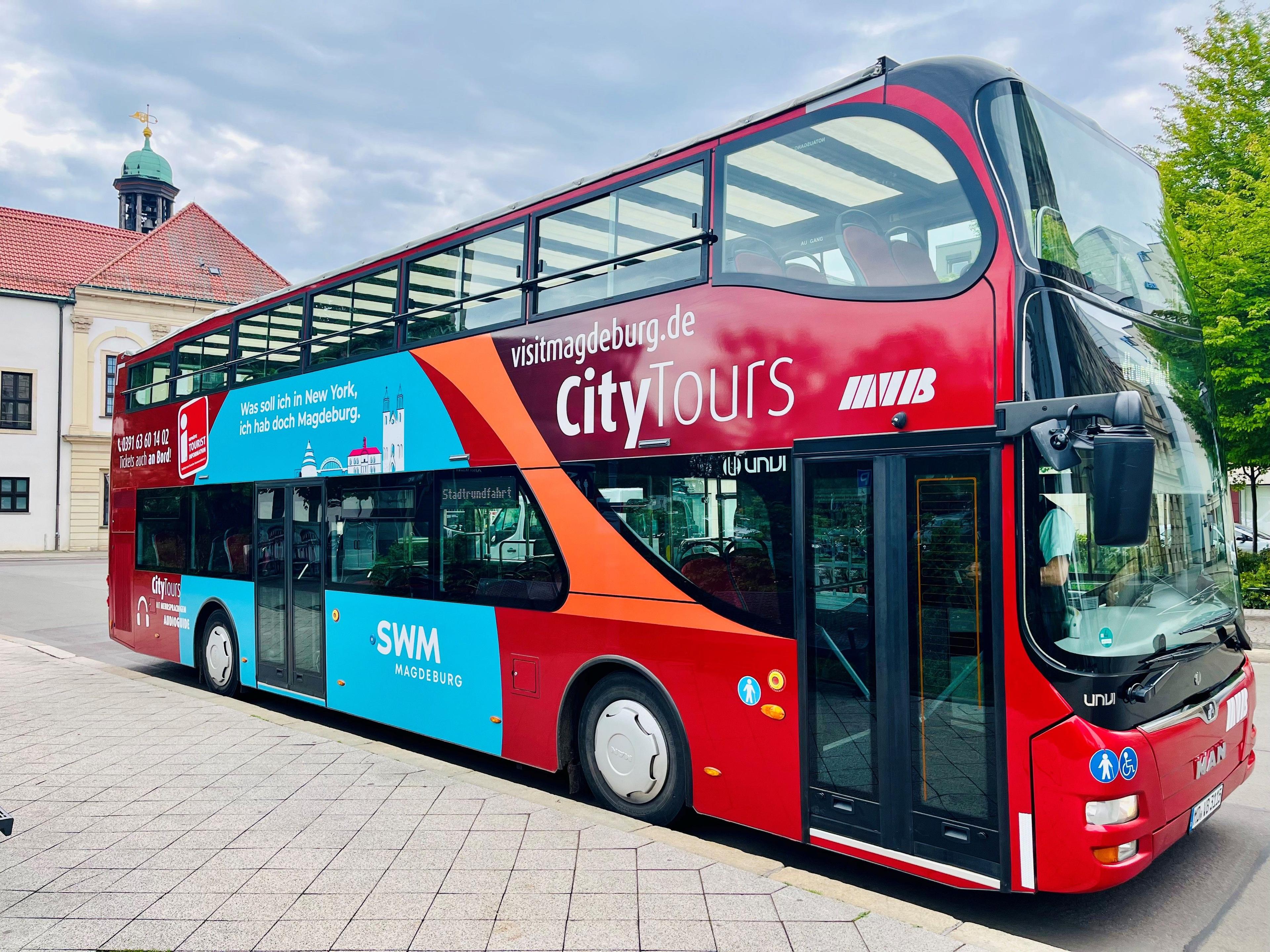 A red double-decker city tour bus with an open top deck parked outside.
